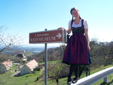 Elani stands outdoors on a sunny day wearing traditional German garb in front of a museum sign.