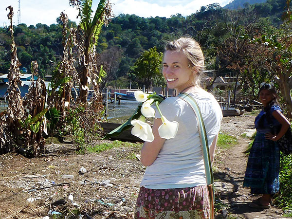 Hillary standing with an armful of calla lillies, looking back over her shoulder, with lush vegetation in the background.