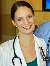 Annaliese is wearing a lab coat with stethoscope around her neck. Her dark brown hair is tightly pulled back, and her dark teal shirt matches her earrings and eyes.
