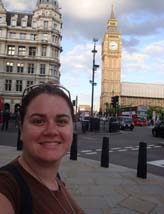 Jennifer smiles in front of a large clock tower and other older city buildings.
