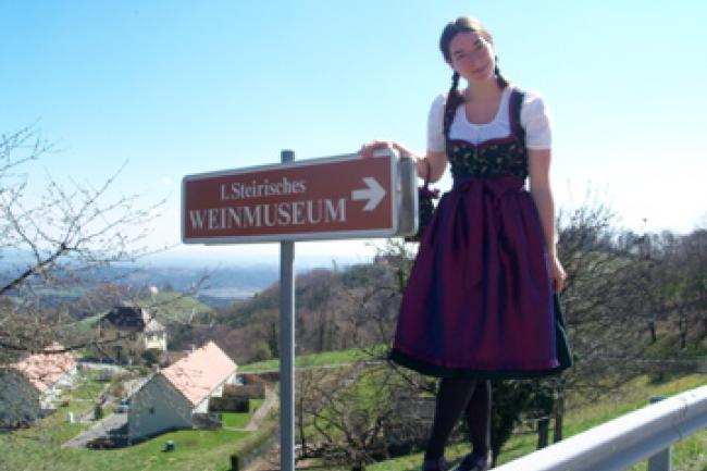 Elani stands outdoors on a sunny day wearing traditional German garb in front of a museum sign.