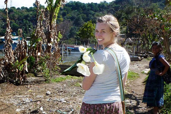 Hillary standing with an armful of calla lillies, looking back over her shoulder, with lush vegetation in the background.