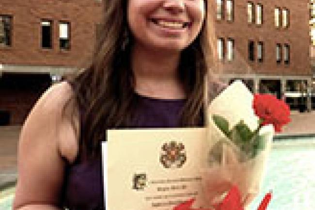 Rebecca smiles in front of Bond Hall and the fountain in Red Square while holding her diploma and a couple white/red roses.