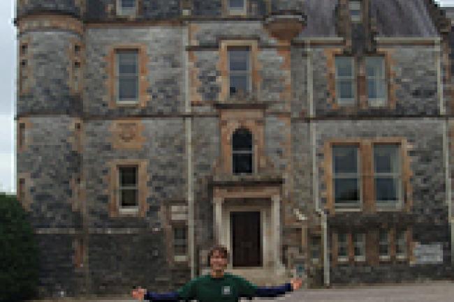 Matt stands in a green sweatshirt with his arms outstretched in front of a castle.